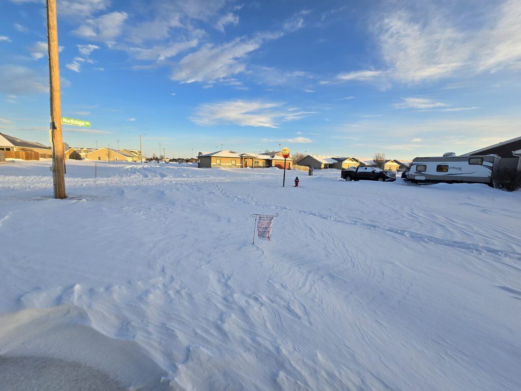 Snowy neighborhood with stop sign and vehicles.