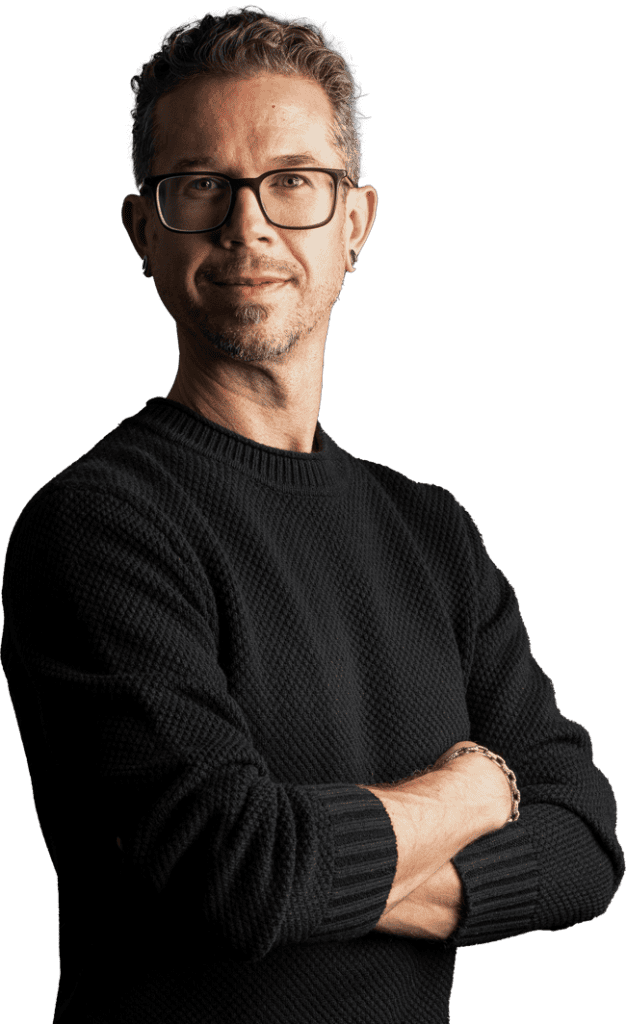 Person wearing glasses smiling against dark background.